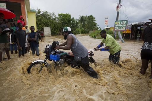 Men push a motorbike through a street flooded by a river that overflowed from heavy rains caused by Hurricane Matthew in Leogane, Haiti, Wednesday, Oct. 5, 2016.  Rescue workers in Haiti struggled to reach cutoff towns and learn the full extent of the death and destruction caused by Hurricane Matthew as the storm began battering the Bahamas on Wednesday and triggered large-scale evacuations along the U.S. East Coast. (AP Photo/Dieu Nalio Chery)
