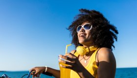 Cheerful african woman drinking yellow cocktail on beach