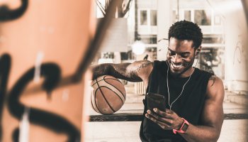 Smiling man with tattoos and basketball using smartphone and earphones