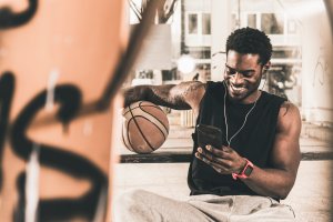 Smiling man with tattoos and basketball using smartphone and earphones