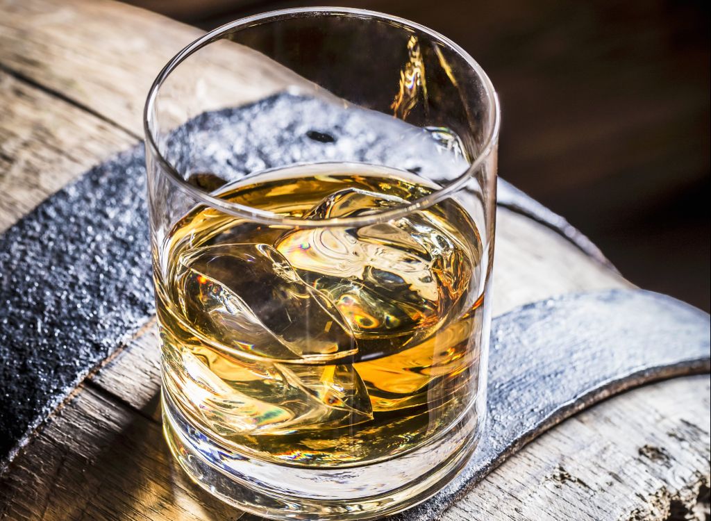 A glass of whiskey with ice on an old wooden barrel