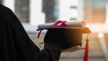 Midsection Of Woman In Graduation Gown Holding Diploma And Mortarboard In City