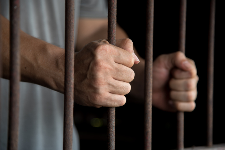 Close-Up Of Man Holding Prison Bars