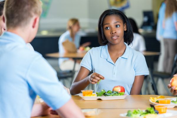 African American teenage girl eats lunch with friends in school cafeteria