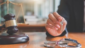 Close-Up Of Judge Holding Keys With Handcuffs On Table