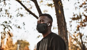 African Male Walking In Park With Face Mask And Listening To Music