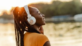 Young African American woman outdoors on sunset and listening music
