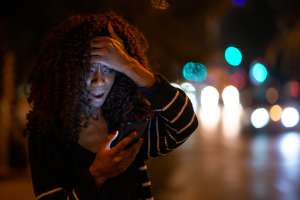 Surprised woman reading bad news on her phone on street at night
