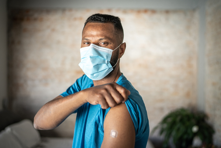 Portrait of a mature man showing arm after vaccination - wearing protective face mask