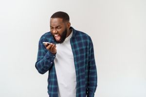 Angry Young Man Shouting On Mobile Phone While Standing Against White Background