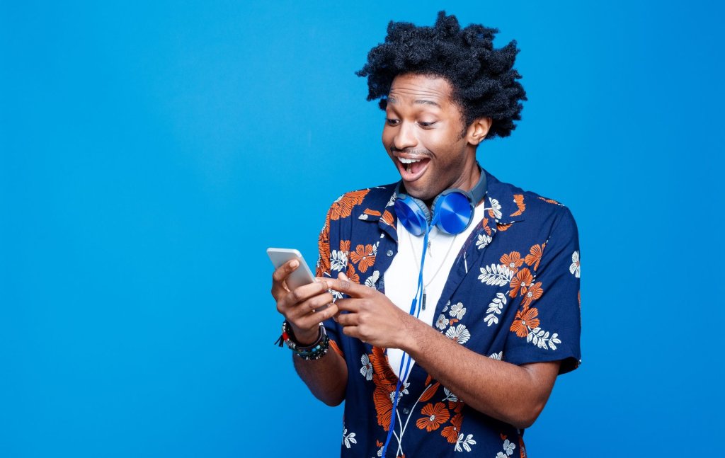 Surprised young man in hawaiian shirt holding smart phone
