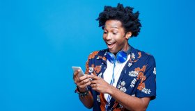 Surprised young man in hawaiian shirt holding smart phone