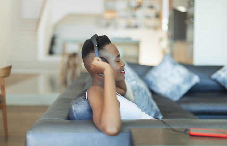 Smiling, serene young woman listening to music with headphones and mp3 player on living room sofa