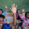 Smiling diverse multi-cultural students raising hands in classroom