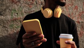 unrecognizable young man with smartphone, coffee cup and headphones - yellow color concept