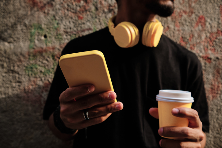 unrecognizable young man with smartphone, coffee cup and headphones - yellow color concept