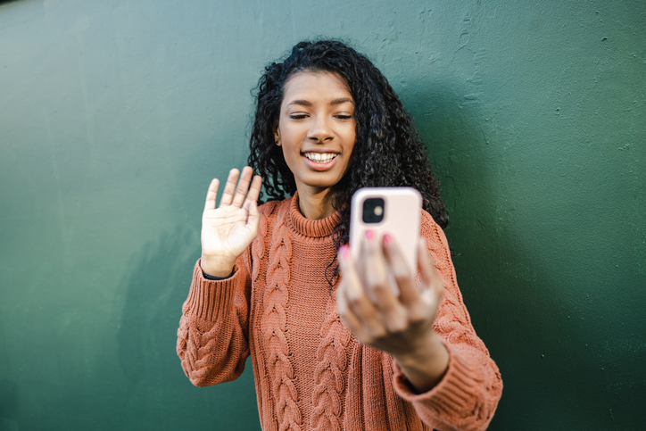 Smiling young African-American woman waving while taking a selfie