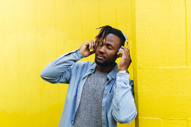 Young man listening music through headphones by yellow wall