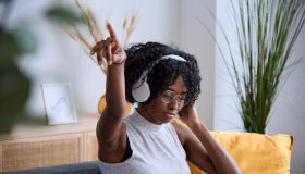 Afro woman enjoying listening music with headphones while relaxing sitting on a sofa at home.