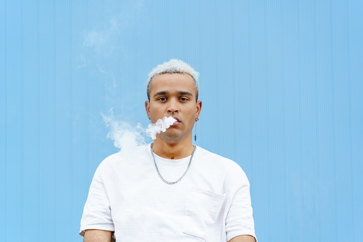 Horizontal portrait of skater hispanic man on his 20s smoking outdoors on blue wall
