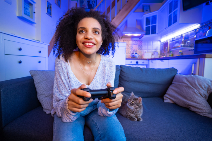 Smiling african-american young woman enjoying videogame on playstation, having fun at home on the evening