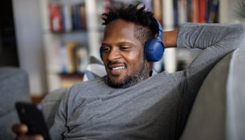 Smiling man with headphones resting on couch and using mobile phone