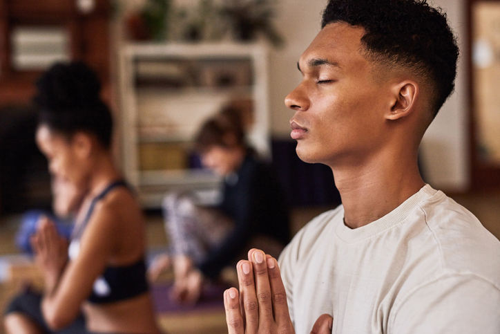 Zen, meditation and spiritual man in a yoga class with eyes closed to focus on mindfulness, breathing and wellness. Pilates, breathe and young person relaxing his healthy body for balance and peace