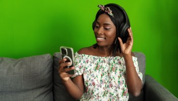 African woman listening to music with headphones while sitting on couch at home