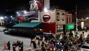 Detroit Will Breathe protesters pass in front of murals in...