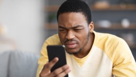 African american guy squinting while using mobile phone
