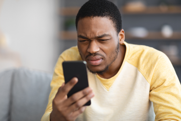 African american guy squinting while using mobile phone