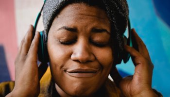 African woman listening music peaceful playlist with headphones outdoors - Urban culture lifestyle concept - Focus on face