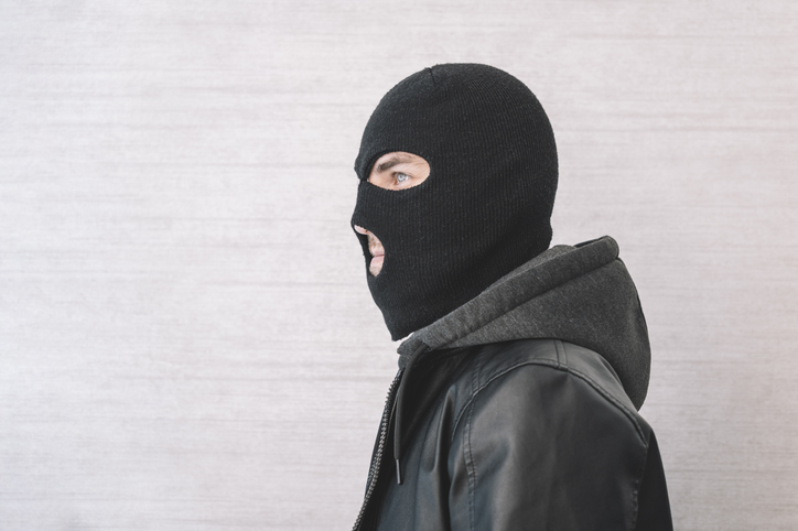thief in a black jacket. A man in a black balaclava with an evil expression on his face. An aggressive bandit on a white background. The concept of crime or theft.