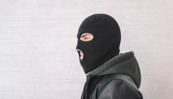 thief in a black jacket. A man in a black balaclava with an evil expression on his face. An aggressive bandit on a white background. The concept of crime or theft.