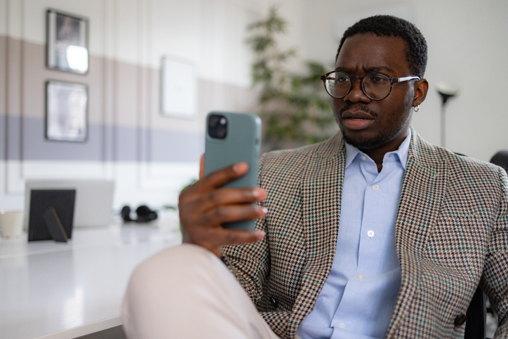 Serious black businessman using smart phone in the office.