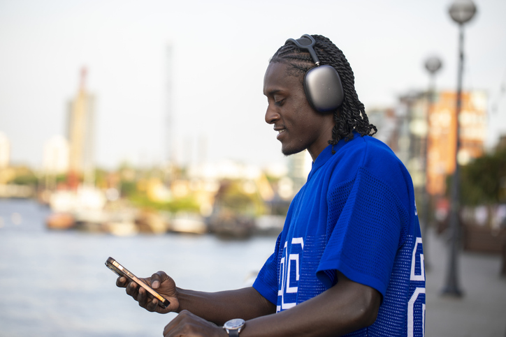 One young man listening to music on headphones and checking a smart phone in the city by a river at twilight