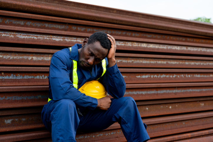 Unemployed blue-collar worker sitting at an industrial site