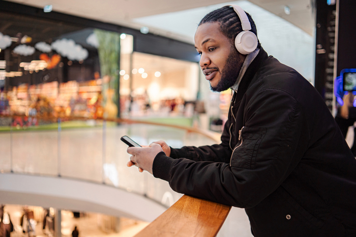 Young adult man listening music with headphones and smartphone in mall