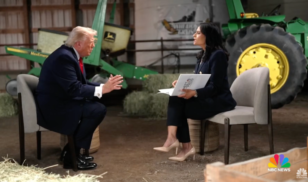 Two people, a man and a woman, sitting and conversing in a room with farm equipment visible in the background.