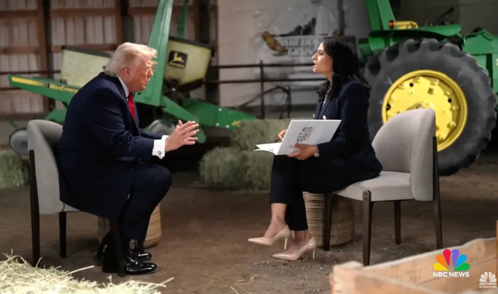 Two people, a man and a woman, sitting and conversing in a room with farm equipment visible in the background.