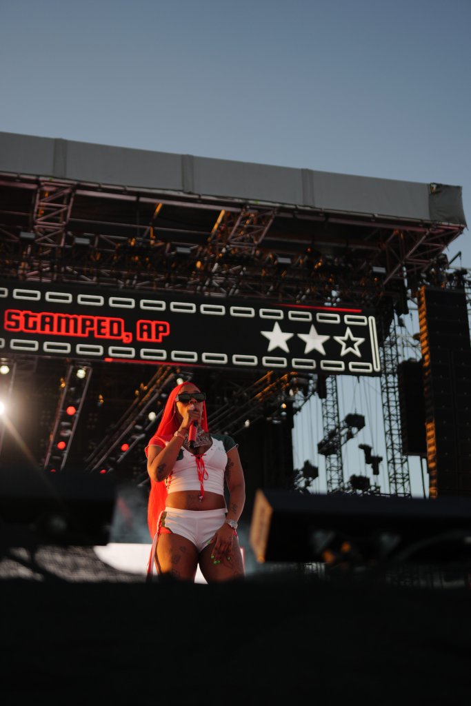 A performer wearing a red outfit stands on a stage with the text "Stamped, AP" displayed above.