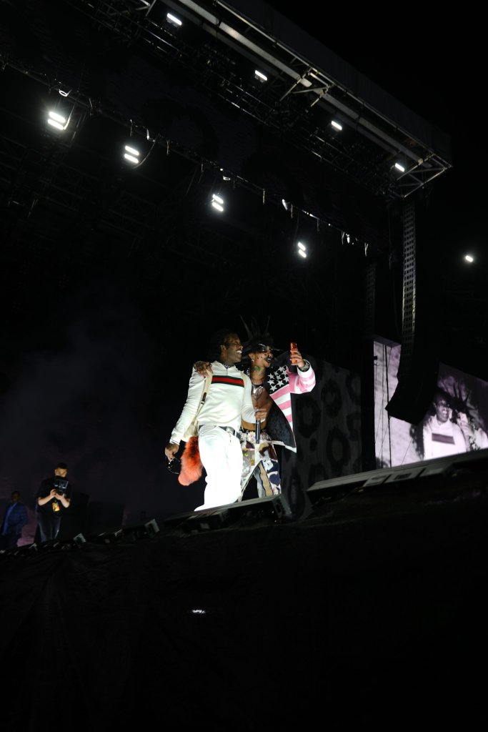 Two performers on a dimly lit stage, one wearing a white and red striped outfit and the other a pink and white outfit with stars, holding microphones and interacting with the audience.