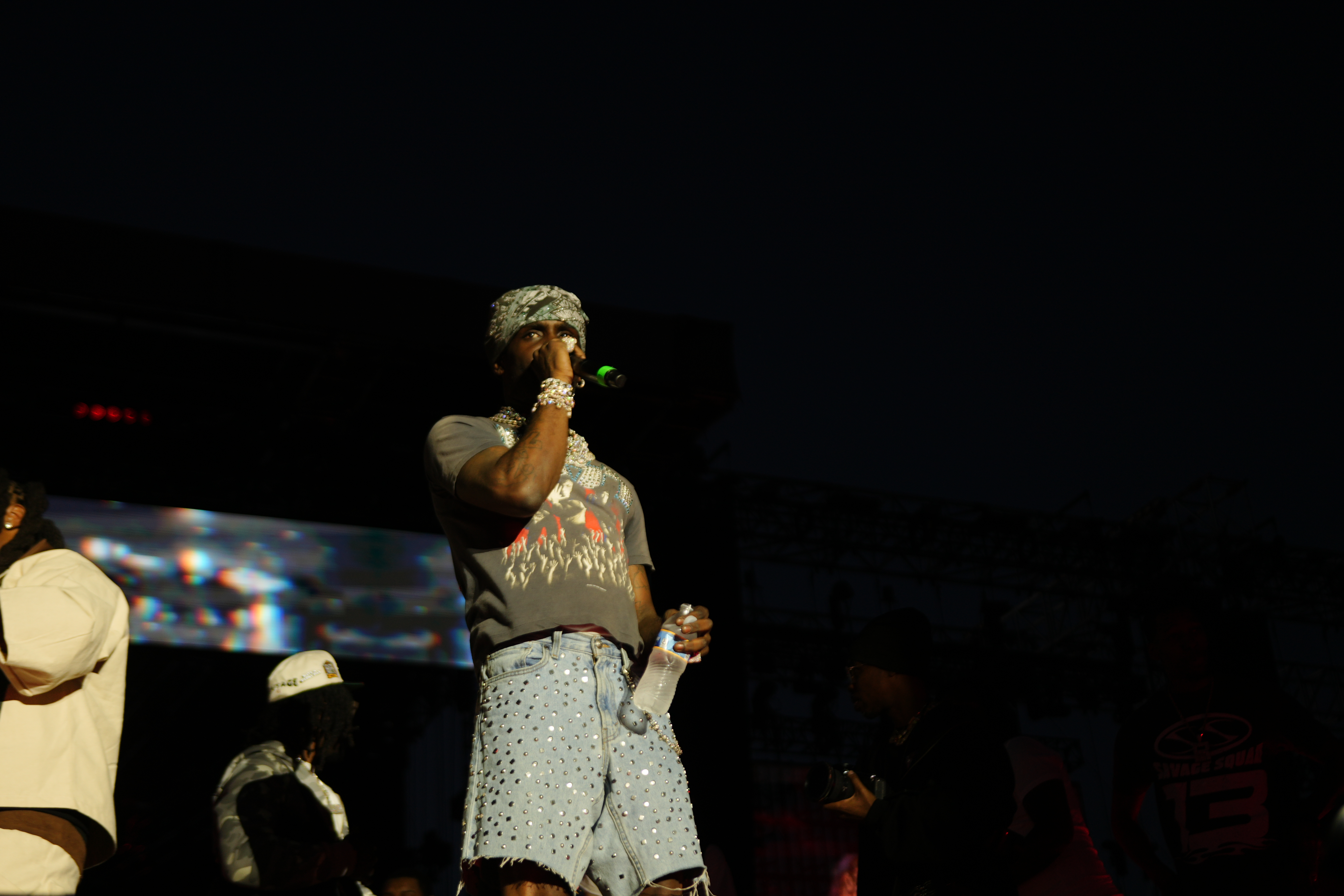 A performer on stage wearing a camouflage hat and patterned outfit, holding a microphone and singing into it.