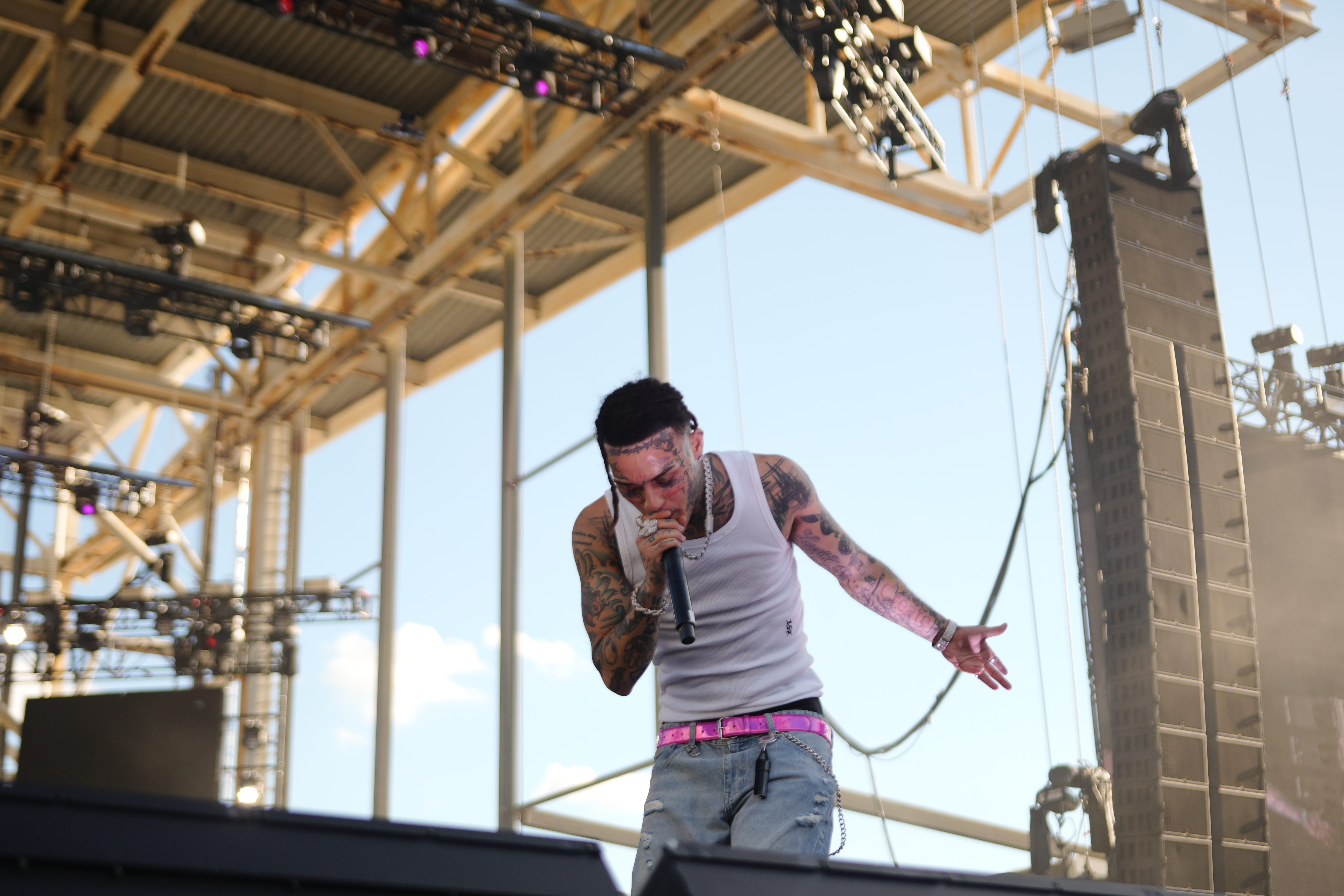A tattooed man performing on stage, holding a microphone and gesturing with his hands.