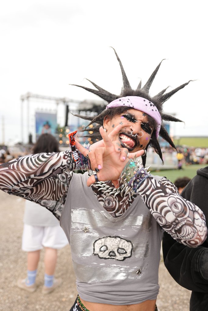 A person with a punk-inspired hairstyle and face paint making an expressive, energetic gesture at an outdoor event or festival.