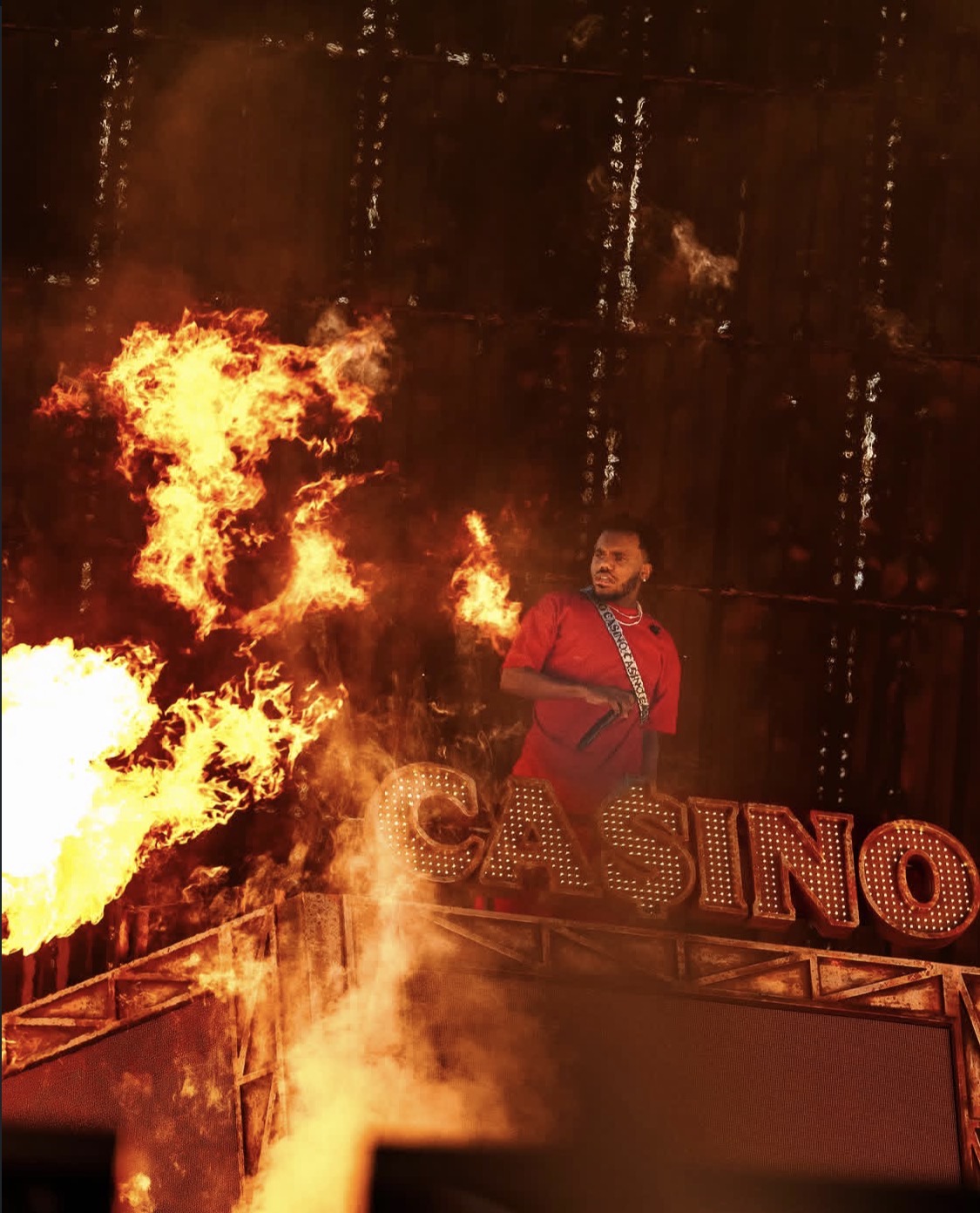 A person in a red costume stands in front of a large flaming "CASINO" sign, surrounded by intense flames and smoke.