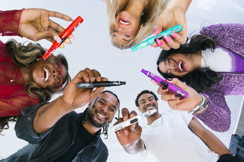 A group of diverse people laughing and holding colorful markers, creating an energetic and playful scene.