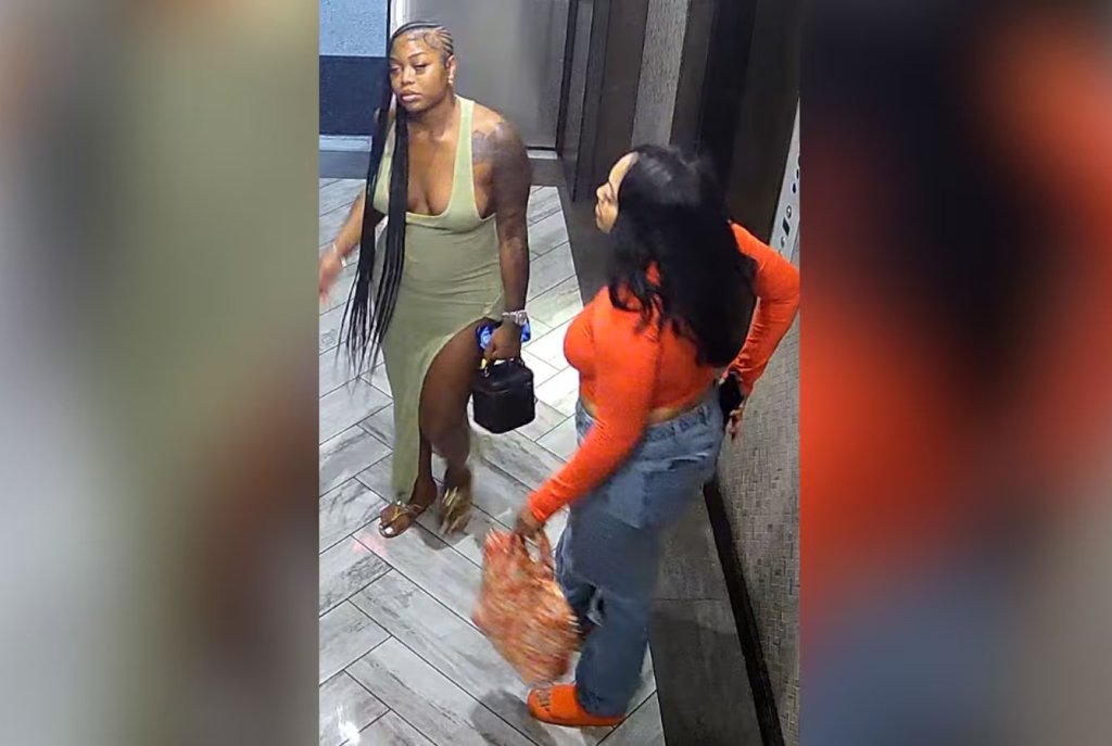 Two people, one wearing an orange outfit and the other wearing a green outfit, standing in a hallway.