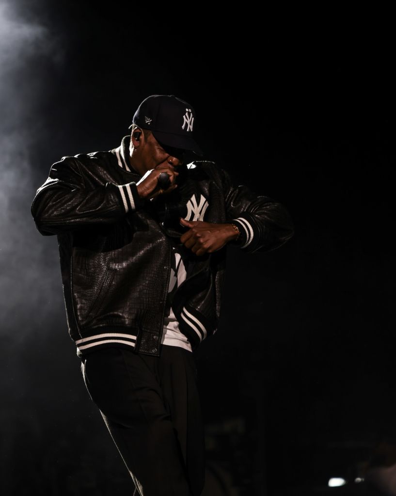 A person wearing a black leather jacket with the "NY" logo, standing in a dark setting and gesturing with their hands.