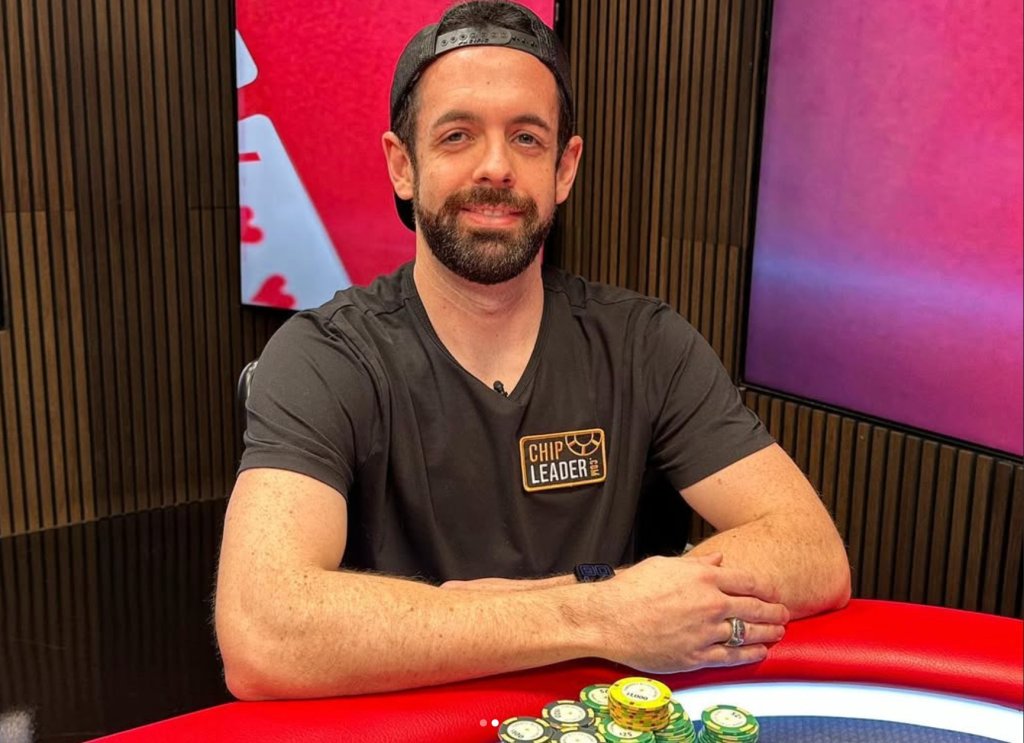 A man with a beard wearing a "Chip Leader" t-shirt sitting at a table with poker chips.